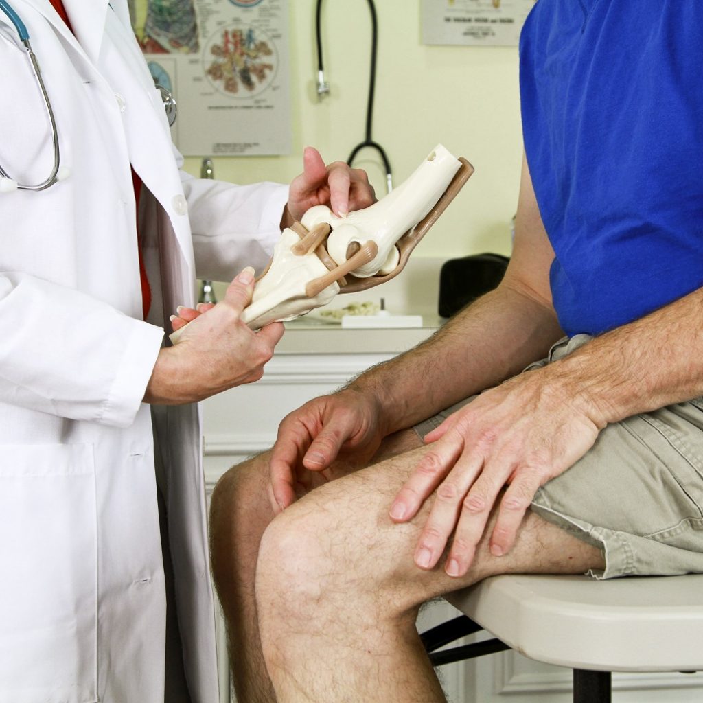 A doctor using a skeletal model of the human knee to explain to her patient the diagnosis of his problem.